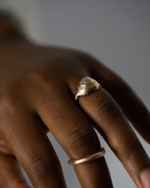 a close up of a hand, wearing a small bronze seashell ring and a small bronze band ring
