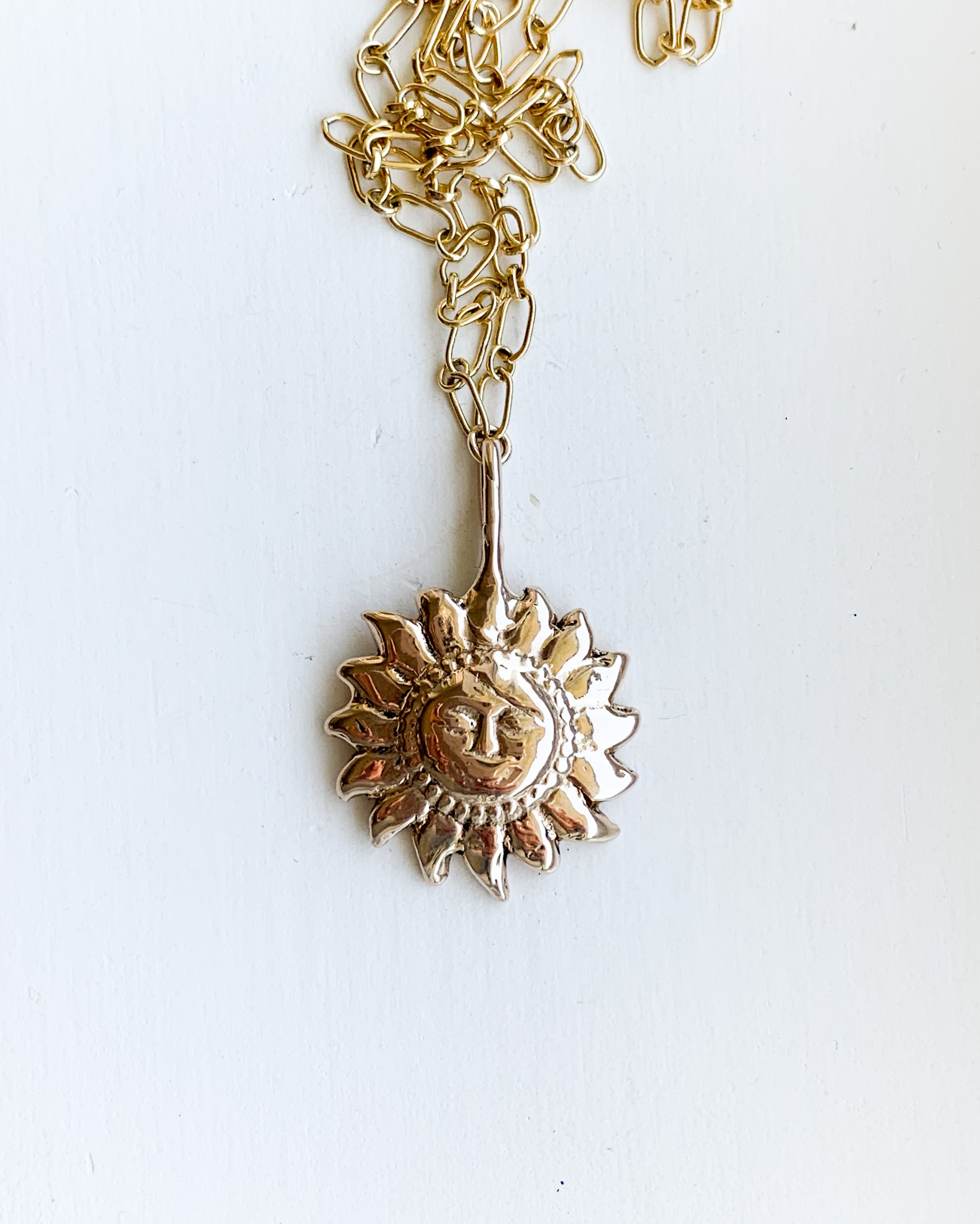 a bronze sun shaped pendant on a gold chain, shown on a white background