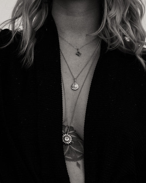 a black and white photo of a woman wearing a black sweater and layered necklaces