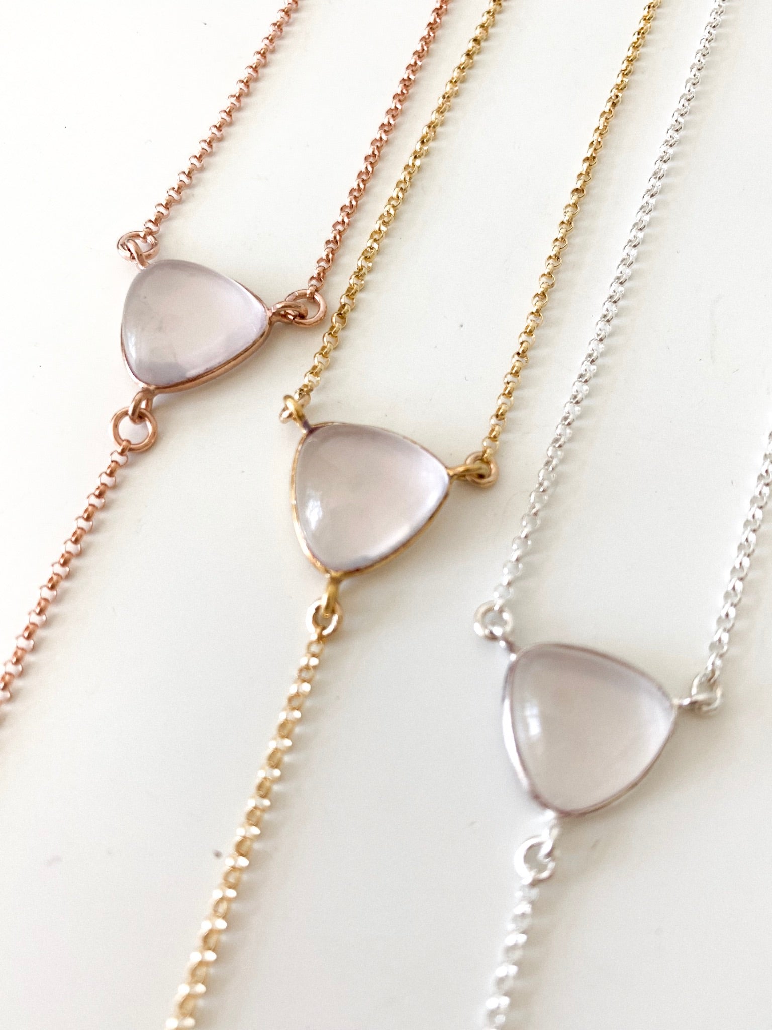 a set of three rose quartz lariat pendants, in rose gold, gold and silver chain styles on a white background