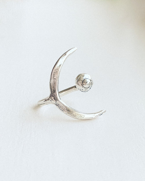a hand formed open silver ring with a small shell on one side and a crescent moon on the other with a white background
