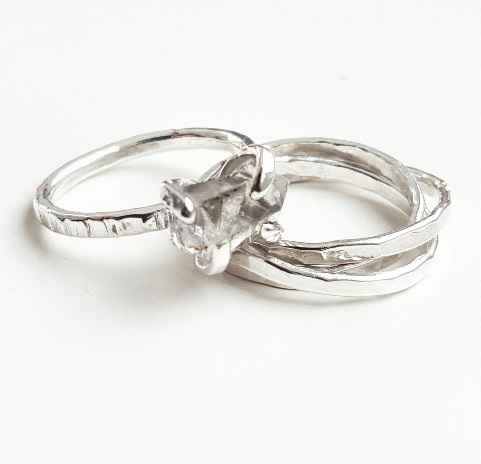 a set of intertwined silver band rings and a silver claw style herkimer diamond ring on a white background