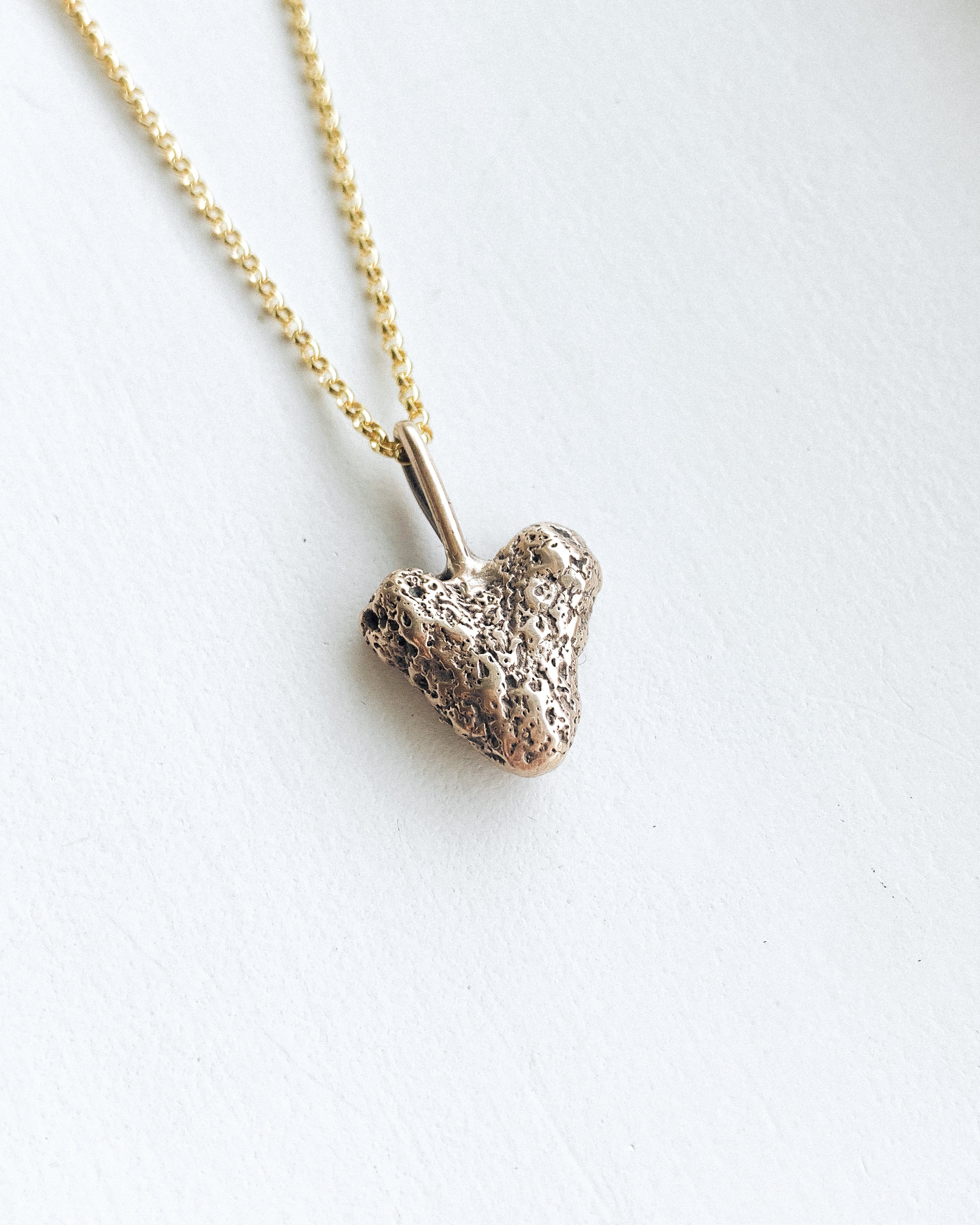 small bronze coral heart pendant with a gold chain on a white background