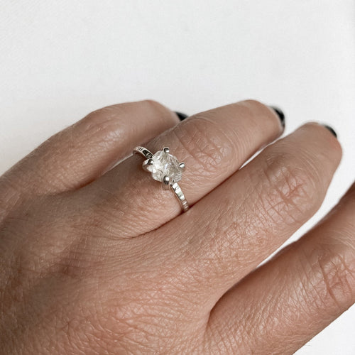 a close up of a finger wearing a silver claw style ring with a herkimer diamond