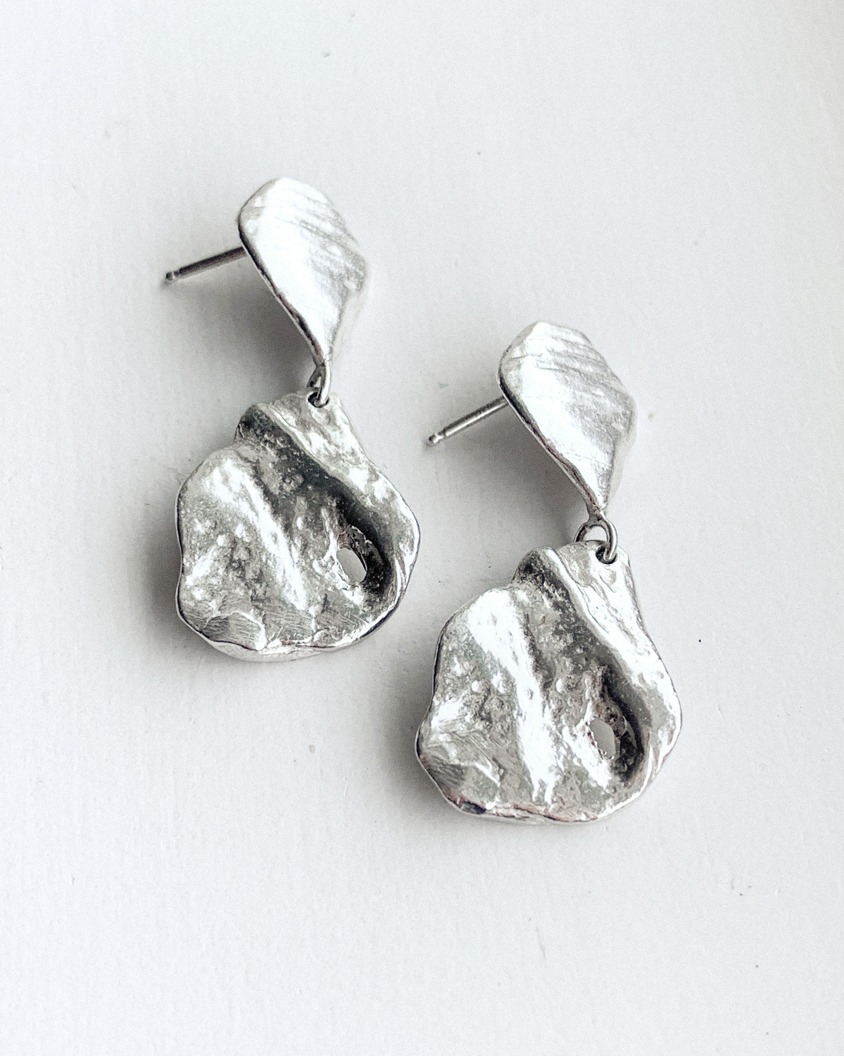 a set of dangly silver sea shell stud earrings shown on a white background